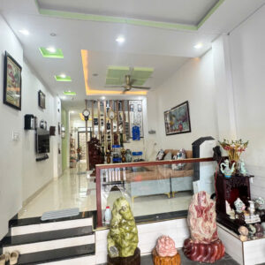 Bright showroom interior with white walls, modern ceiling lights, and a glass railing; foreground shows three large carved stone sculptures on wooden bases.