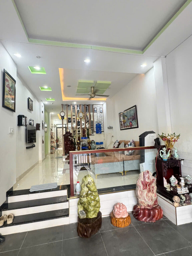 Bright showroom interior with white walls, modern ceiling lights, and a glass railing; foreground shows three large carved stone sculptures on wooden bases.