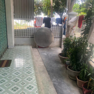 Patio area with green patterned floor tiles, clothes hanging to dry on a line, and a large circular satellite dish in front of a metal fence.