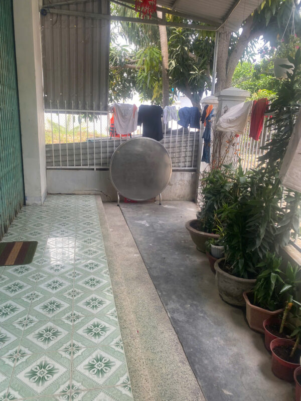 Patio area with green patterned floor tiles, clothes hanging to dry on a line, and a large circular satellite dish in front of a metal fence.