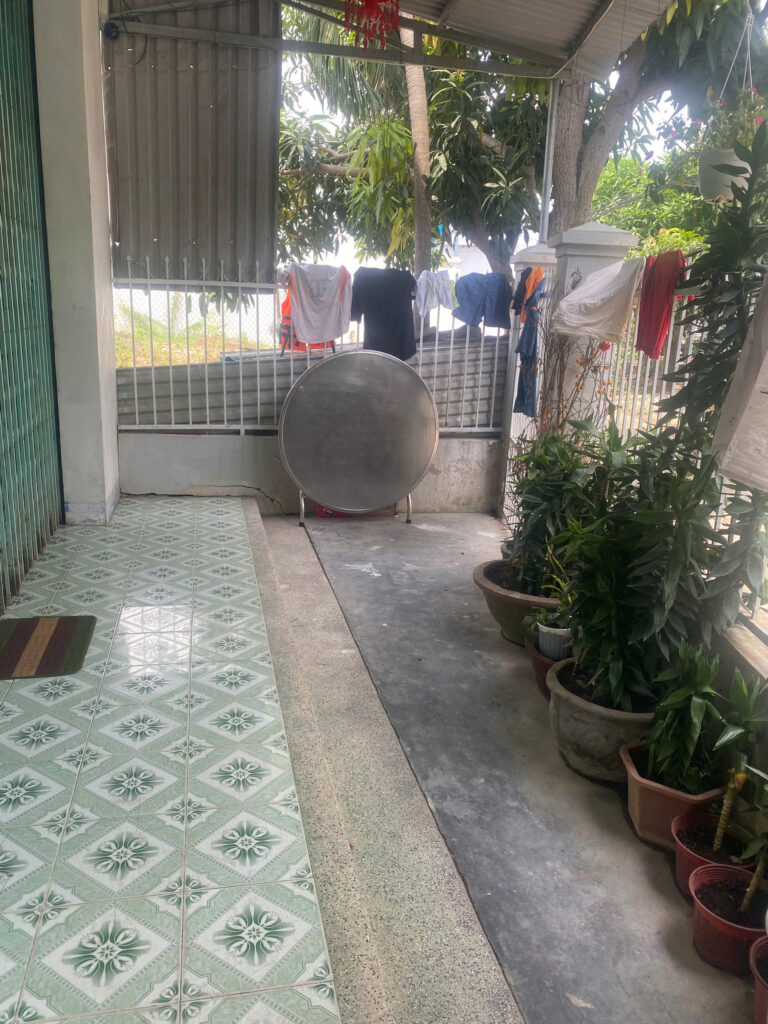 Patio area with green patterned floor tiles, clothes hanging to dry on a line, and a large circular satellite dish in front of a metal fence.