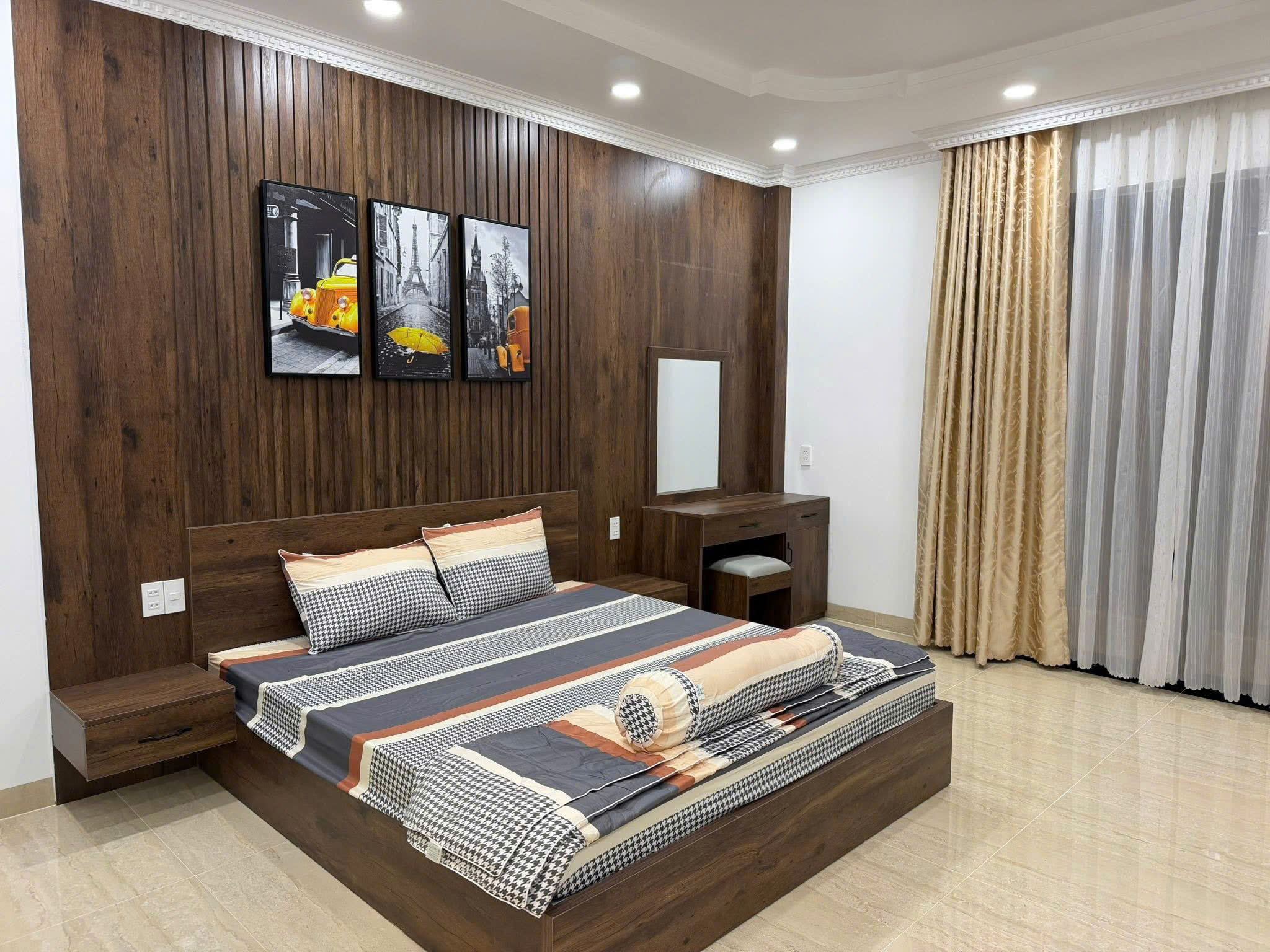 Wood-paneled wall with a low platform bed and matching nightstands in a modern bedroom; three Paris-themed black-and-yellow art prints above the headboard.