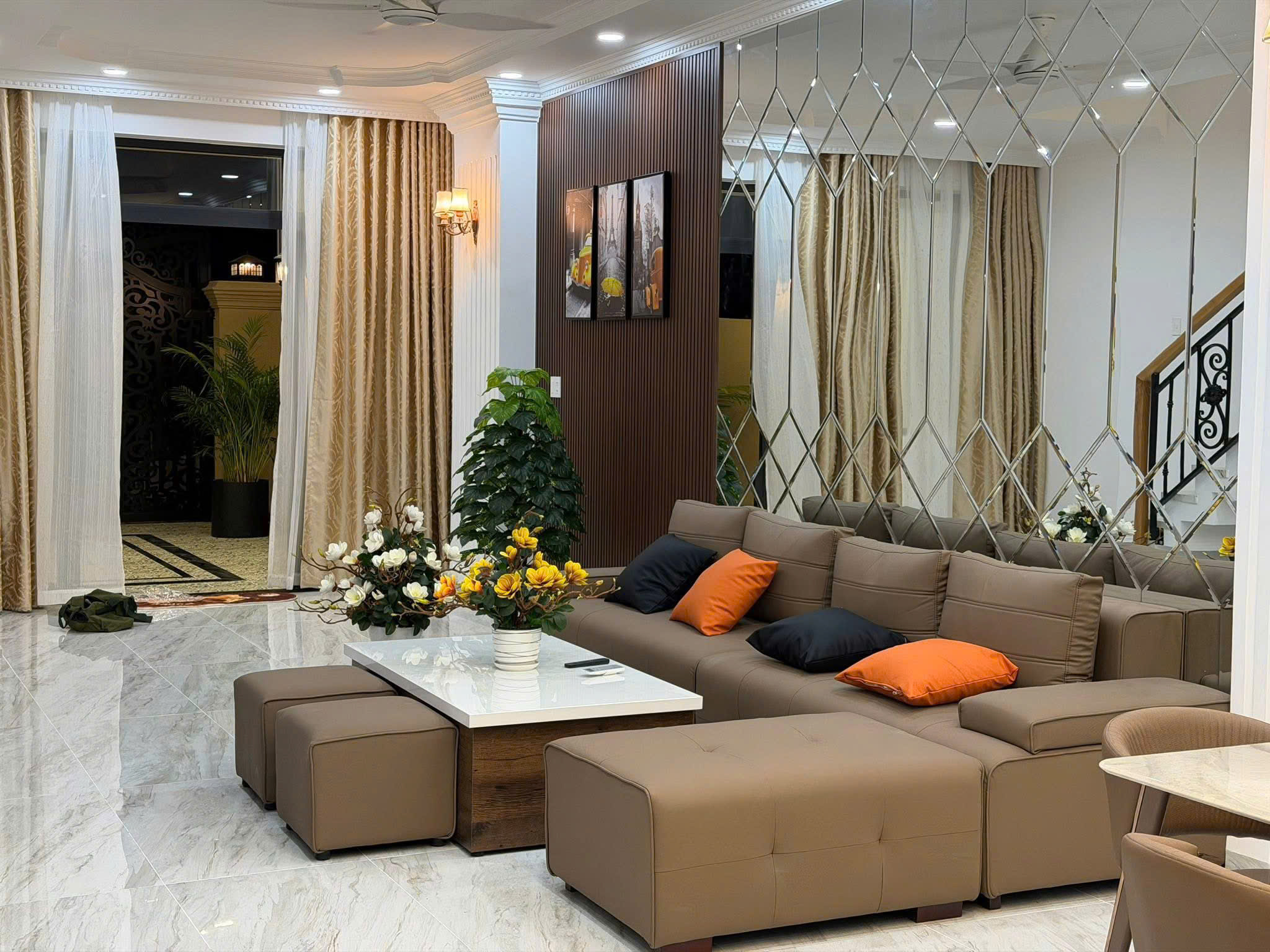 Modern living room with a brown sectional sofa, orange/black pillows, and a white marble coffee table.