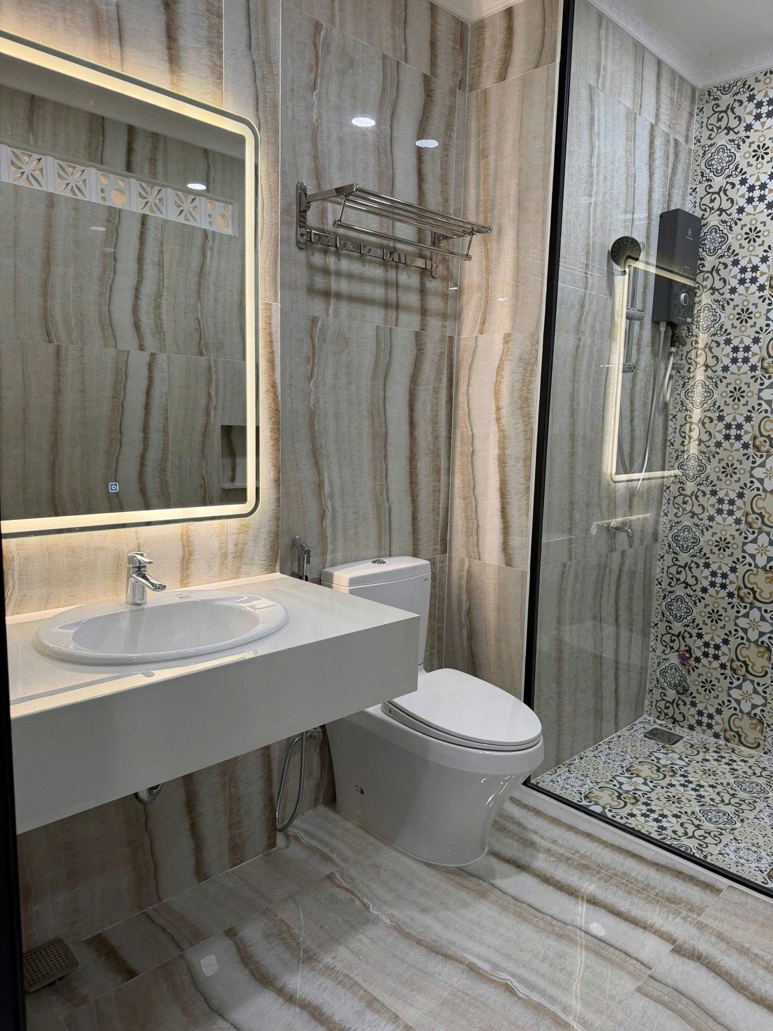 Modern bathroom featuring a wall-mounted sink with chrome faucet, toilet, and glass shower with patterned tile walls.