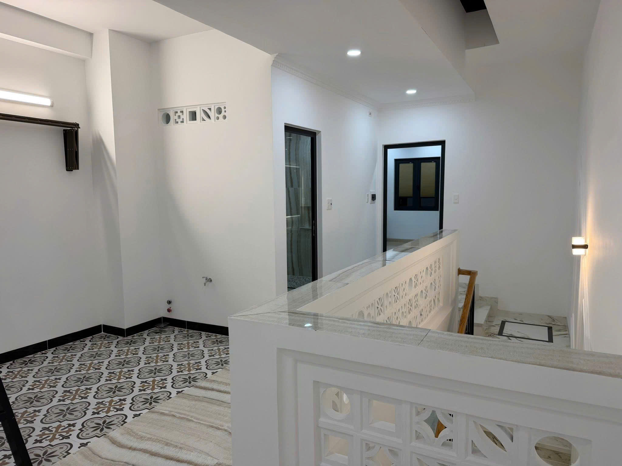 Bright white interior hallway with a patterned tile floor, glass railing, and decorative lattice panels along a stairway.