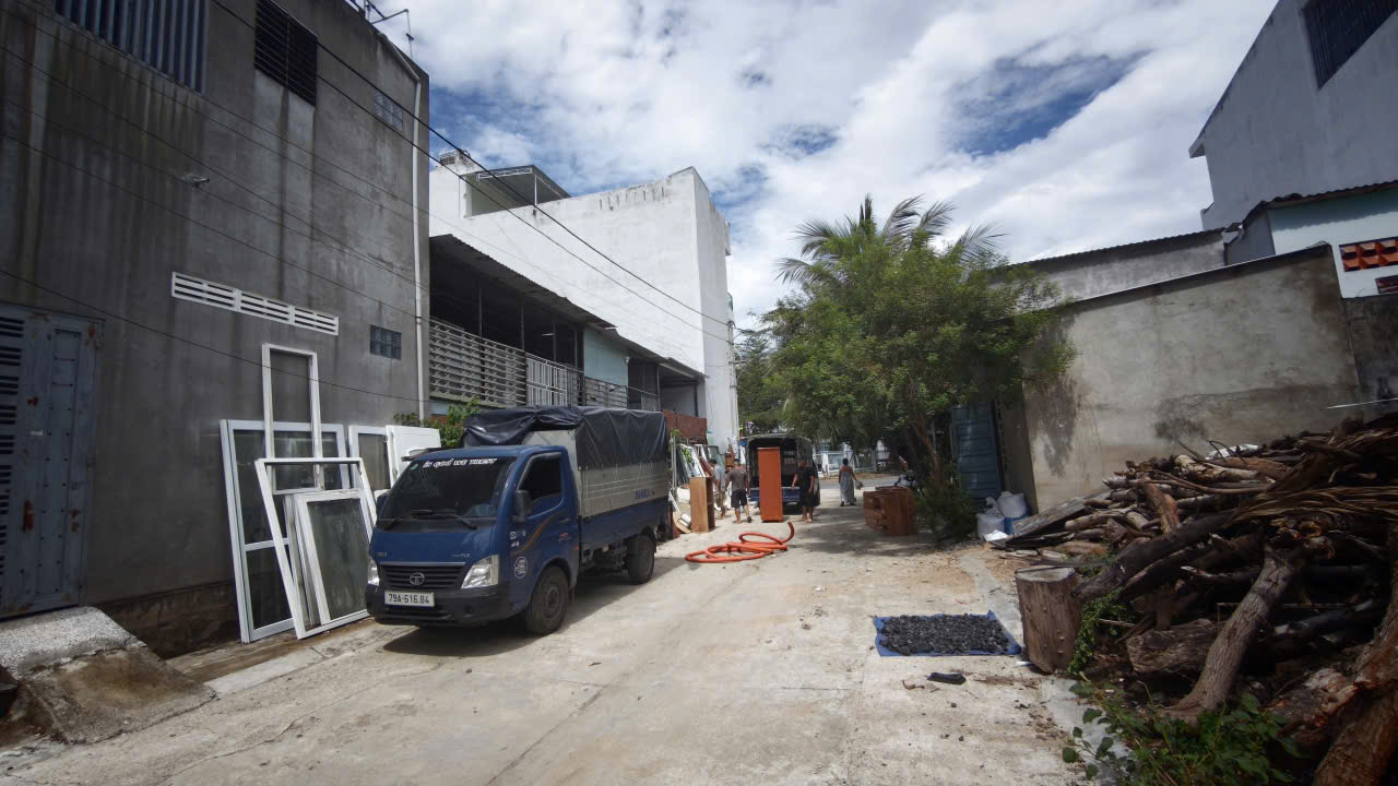 Construction alley with a blue truck and building materials along a concrete road under a cloudy sky.