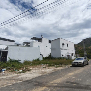 Street view of a quiet residential area with white modern buildings, a parked silver car, and hills in the background under a cloudy sky.