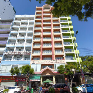 Colorful multi-storey hotel building with pastel facades on a busy urban street, storefronts and parked cars.